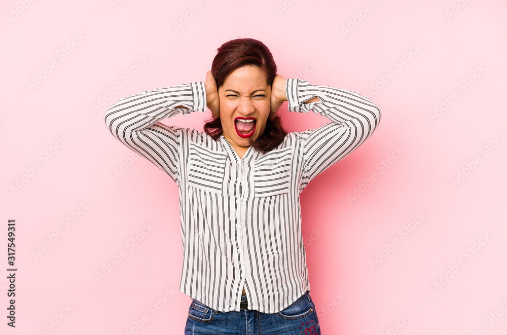 Middle age latin woman isolated on a pink background covering ears with hands trying not to hear too loud sound. Middle age latin woman isolated on a pink background covering ears with hands trying not to hear too loud sound.