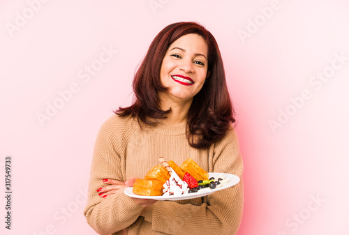 Middle age latin woman holding a waffle isolated laughing and having fun.