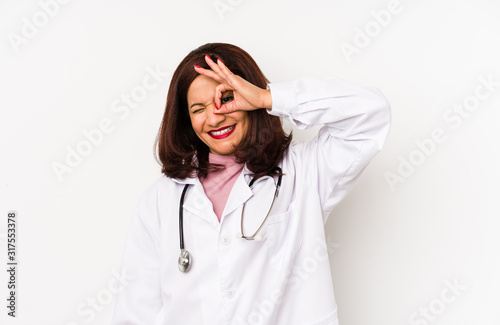 Middle age latin doctor woman isolated excited keeping ok gesture on eye.