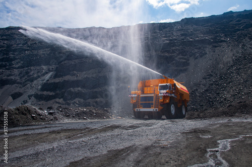 Heavy truck pours the road with water in the iron ore quarry. Dust removal, protection of the environment. Irrigation of the road from dust © Yevhen