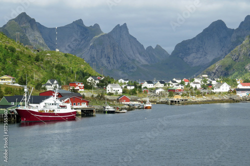 View of ships and litle red and white houses in the Reine bay in front of the impressive mountain landscape of Moskenes, Lofoten Islands, Norway, Europe