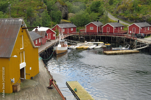 View on the little bay of Nusfjord with yellow and red wooden huts (rorbuers) around a litle harbor with boats; Vestvagoy, Lofoten Islands, Norway, Europe