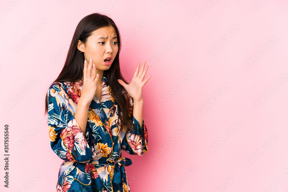 Young chinese woman wearing a kimono pajama isolated shouts loud, keeps eyes opened and hands tense.