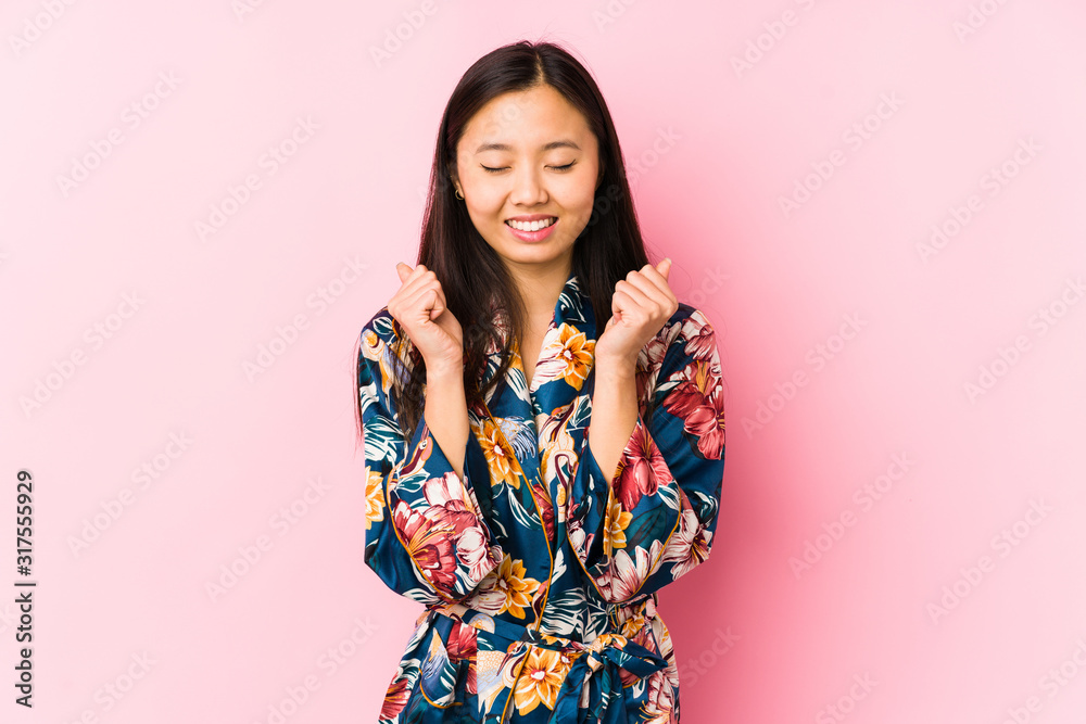 Young chinese woman wearing a kimono pajama isolated raising fist, feeling happy and successful. Victory concept.