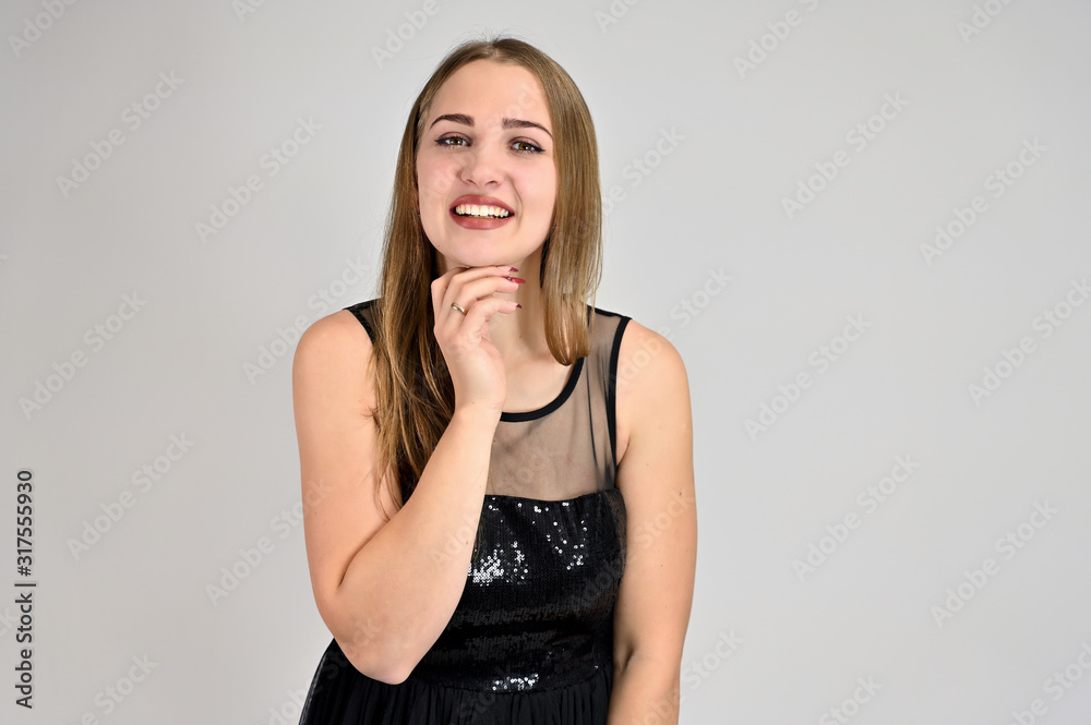Fototapeta premium Universal concept horizontal portrait of a woman on a white background. A photo of a pretty smiling girl with long hair and excellent make-up in a black dress stands in different poses.