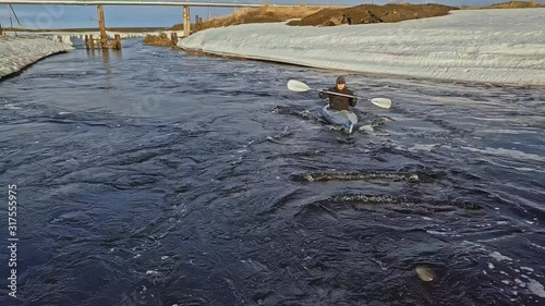 skilled man silhouette sails in canoe upstream between frozen river banks and brown meadows against gaspipe photo