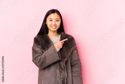 Young chinese woman wearing a coat isolated smiling and pointing aside, showing something at blank space. © Asier