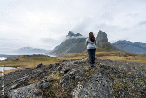 Girl in hiker clothes are looking towards the famous Eystrahorn mountain chains in the background. Hvalnes peninsula in Iceland. Hiking and explorer concept.