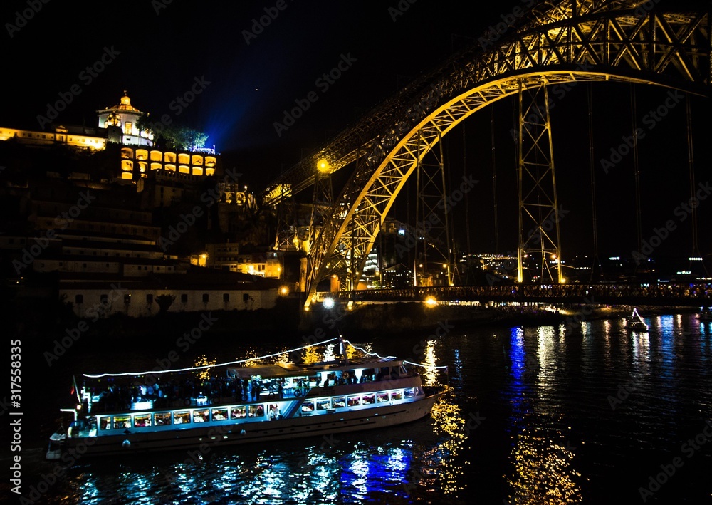 Portugal, evening Porto, lights of night city, night view of The Eiffel Bridge in Porto, Ponte Dom Luis,  Bridge Ponti Di Don Luis, Passenger boat floats under the bridge at night, Douro river