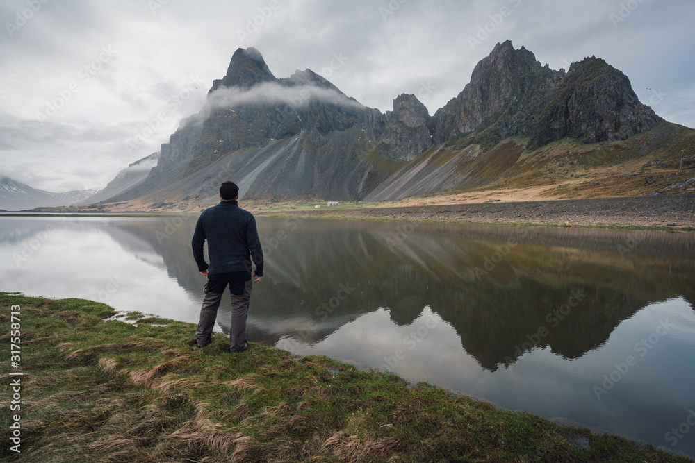 Man looking towards the beautiful mountains of Eystrahorn which reflects in the water. Peace of mind, soulfulness and nature concept.
