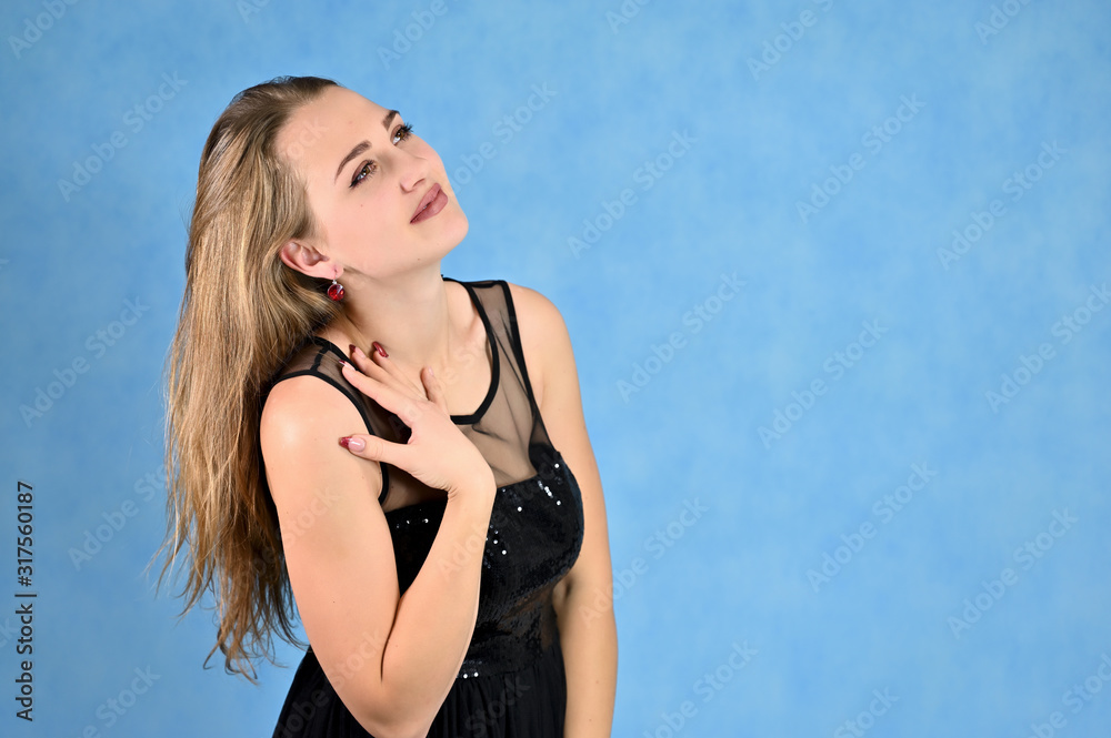 A photo of a pretty smiling girl with long hair and excellent make-up in a black dress stands in different poses. Universal concept horizontal portrait of a woman on a blue background. A photo of a pretty smiling girl with long hair and excellent make-up in a black dress stands in different poses. Universal concept horizontal portrait of a woman on a blue background.