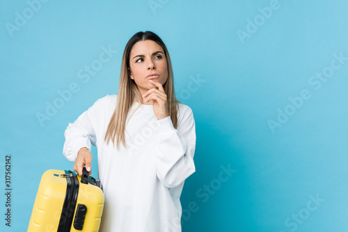 Young caucasian woman holding a suitcase looking sideways with doubtful and skeptical expression. photo