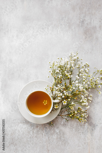 Cup of tea with white flowers on textured background. Top view, blank space