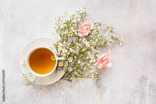 Cup of tea surrounded by various flowers on rustic gray background. Top view, blank space
