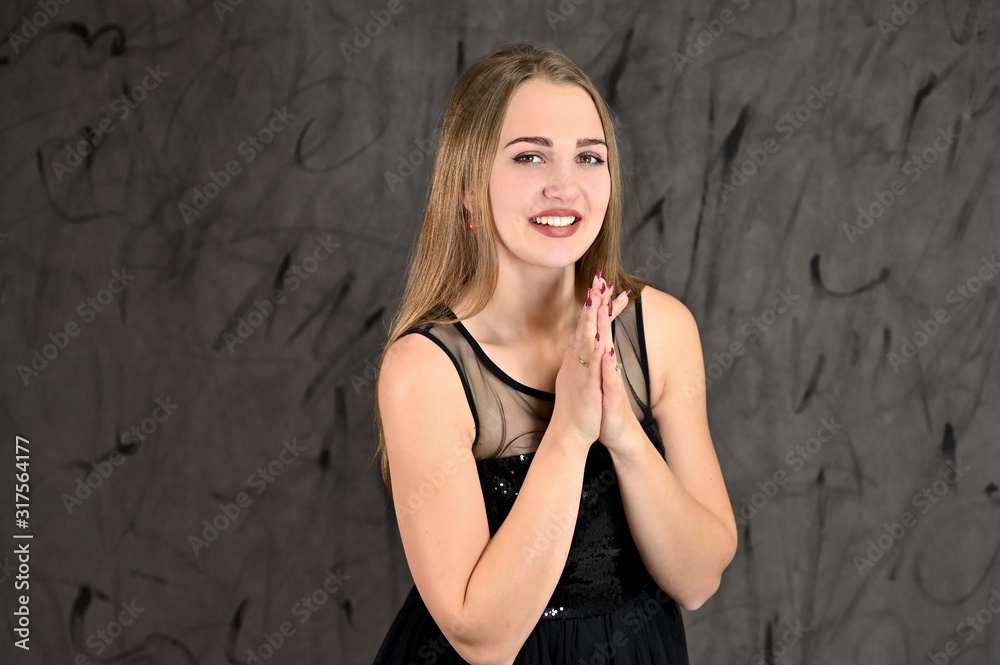 Universal concept of horizontal female portrait on gray alternative background. A photo of a pretty smiling girl with long hair and excellent make-up in a black dress stands in different poses.