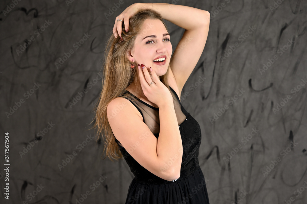 A photo of a pretty smiling girl with long hair and excellent make-up in a black dress stands in different poses. Universal concept of horizontal female portrait on gray alternative background. A photo of a pretty smiling girl with long hair and excellent make-up in a black dress stands in different poses. Universal concept of horizontal female portrait on gray alternative background.