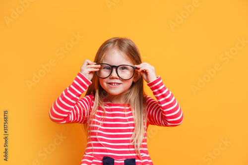 Portrait of young smiling girl wearing glasses on yellow background