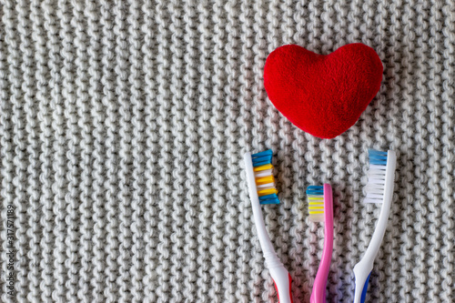 Three toothbrushes and a red heart on a knitted gray background. Two adults, one children's toothbrush and heart. Love, family concept and valentines day, family with a child. Copy space