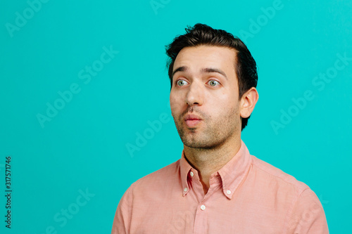 Portrait of a young adult man making funny faces, isolated on blue studio background