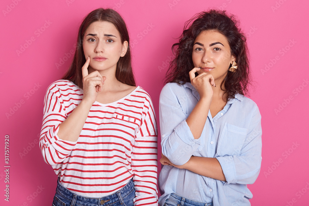 Portrait of pensive magnetic beautiful females thinking over, putting fingers close to mouths, wearing striped sweatshirt, blue shirt and jeans, having thoughtful look. Communication concept. Portrait of pensive magnetic beautiful females thinking over, putting fingers close to mouths, wearing striped sweatshirt, blue shirt and jeans, having thoughtful look. Communication concept.