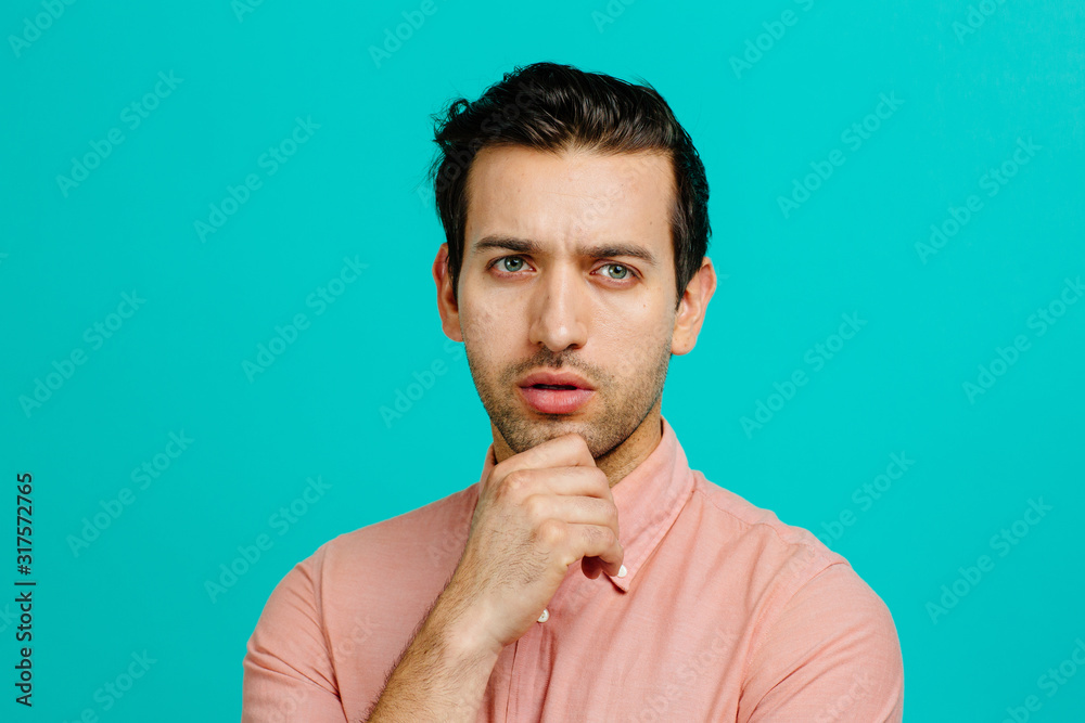 Close up headshot portrait of a young adult man with his hand on his chin, isolated on blue studio background Close up headshot portrait of a young adult man with his hand on his chin, isolated on blue studio background