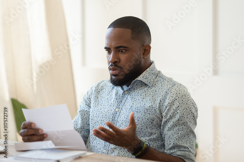 African man sitting at table holding letter reading awful news photo