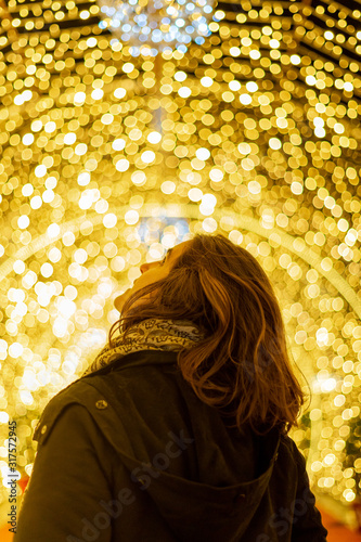 Girl seen from behind looking up with christmas lights in the background