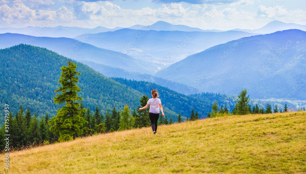 Girl walking on the lawn on the background of majestic blue mountains_