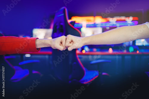 Professional gamer greeting and support team fists hands online game in neon color blur background. Soft focus, back view