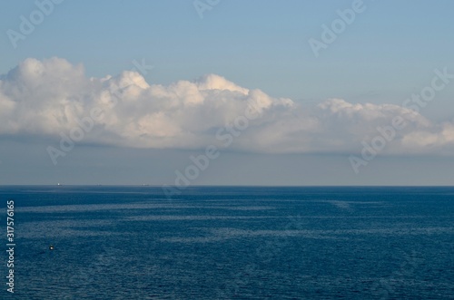 Black sea of blue in calm weather with white clouds with three barges on the horizon and a fishing boat with fishermen.