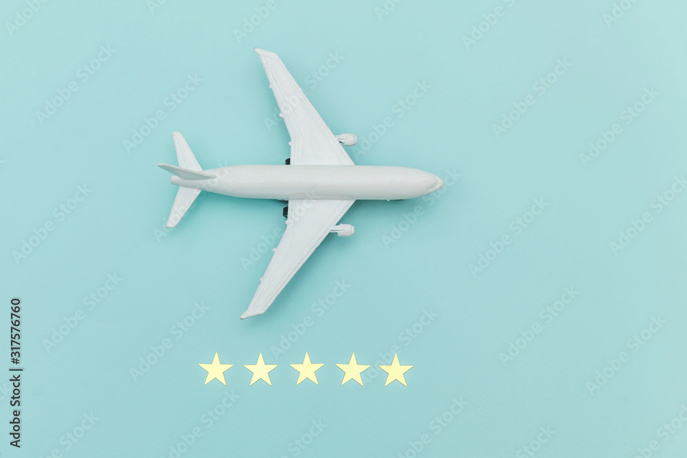 Simply flat lay design miniature toy model plane and 5 stars rating on blue pastel colorful trendy background. Travel by plane vacation summer weekend sea adventure trip journey ticket tour concept.
