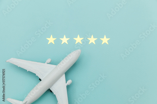 Simply flat lay design miniature toy model plane and 5 stars rating on blue pastel colorful trendy background. Travel by plane vacation summer weekend sea adventure trip journey ticket tour concept.