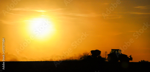 Photo Silhouette of a tractor sowing seeds in a field in a cloud of dust against the background of the setting sun