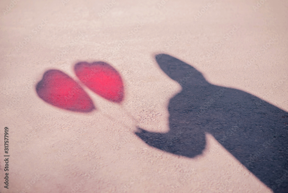Shadow of male figure with two red balloons shaped like heart. Silhouette of man with red hearts on grey tarmac in sunny day. Secret adorer or lover, stalking and danger concept