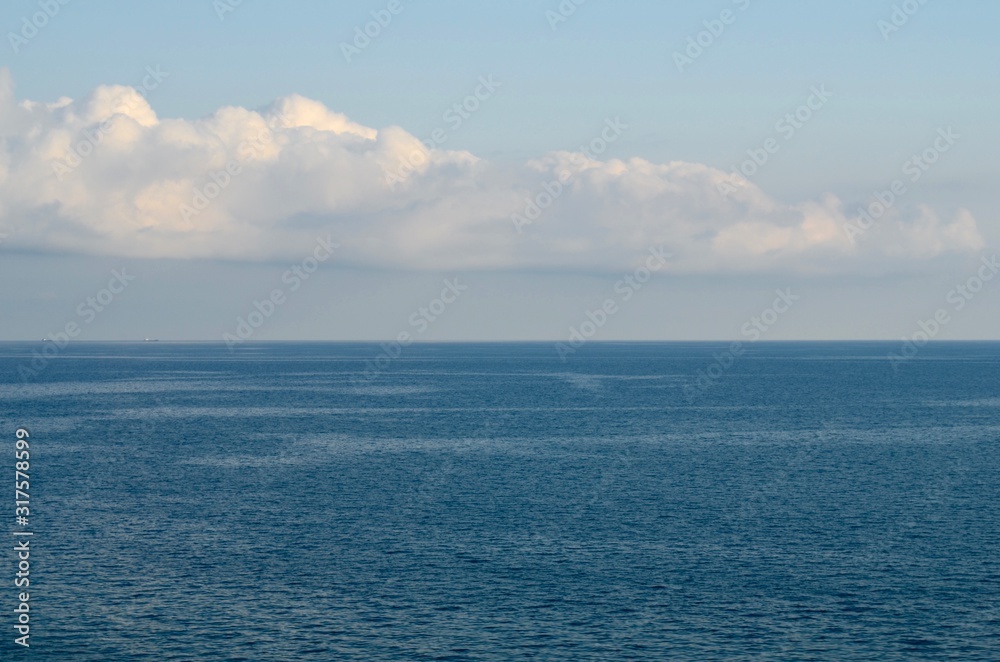 The black sea is blue with a blue sky and a white cloud and two barges floating on the horizon.