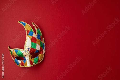 Festive, colorful mardi gras or carnivale mask and accessories over red background. Party invitation, greeting card, venetian carnivale celebration concept. Flat lay, top view, copy space