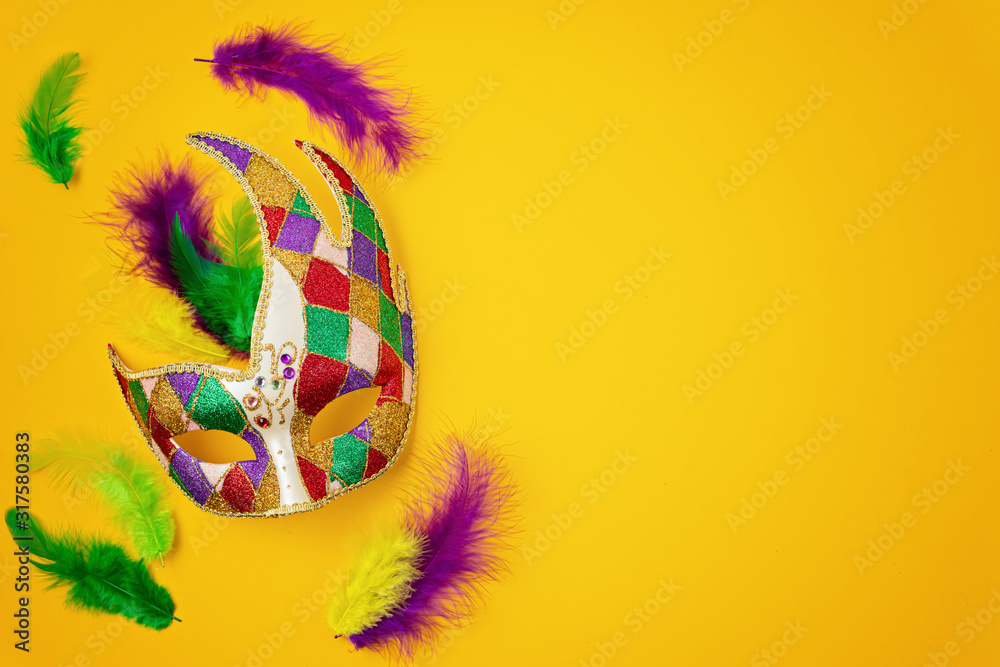 Festive, colorful mardi gras or carnivale mask and accessories over yellow background. Party invitation, greeting card, venetian carnivale celebration concept. Flat lay, top view, copy space - obrazy, fototapety, plakaty 