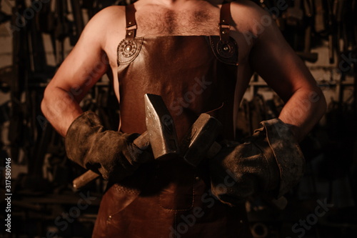 Brutal artisan blacksmith standing in a workshop with two hammers close up © pantovich