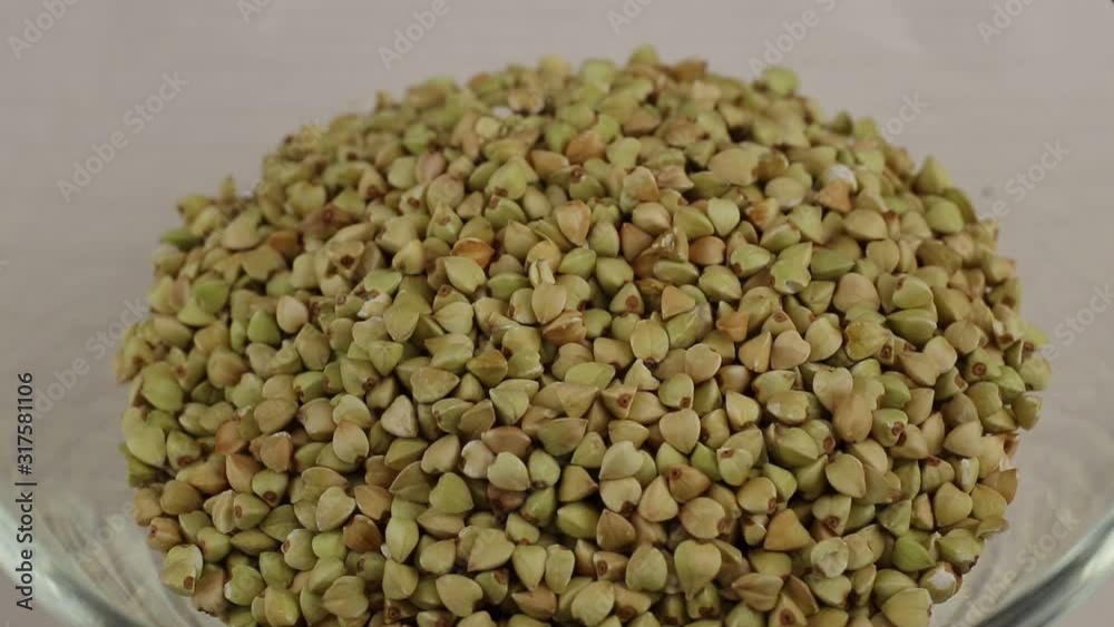 Green buckwheat kernels fall in a glass transparent bowl, close-up Green buckwheat kernels fall in a glass transparent bowl, close-up