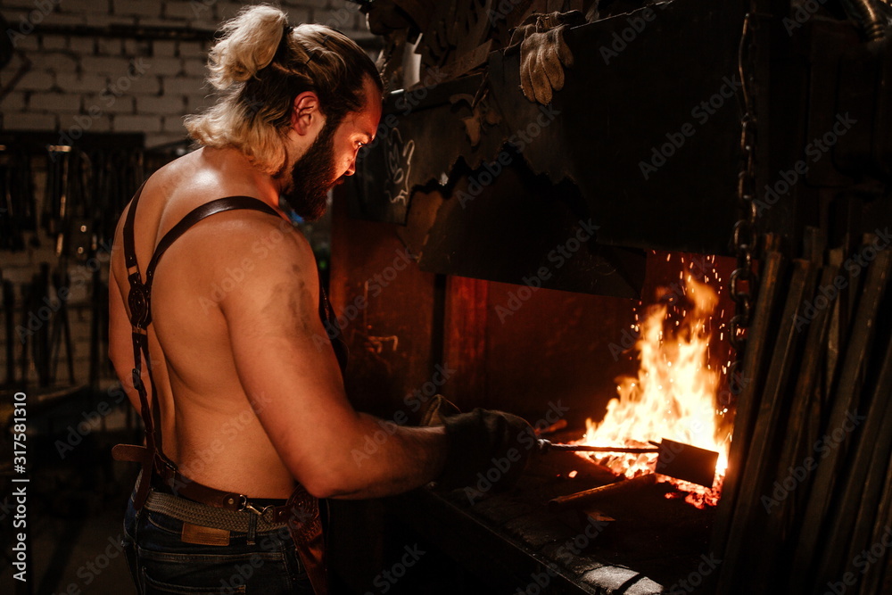 Brutal bearded man in an apron, heats iron in the oven Brutal bearded man in an apron, heats iron in the oven