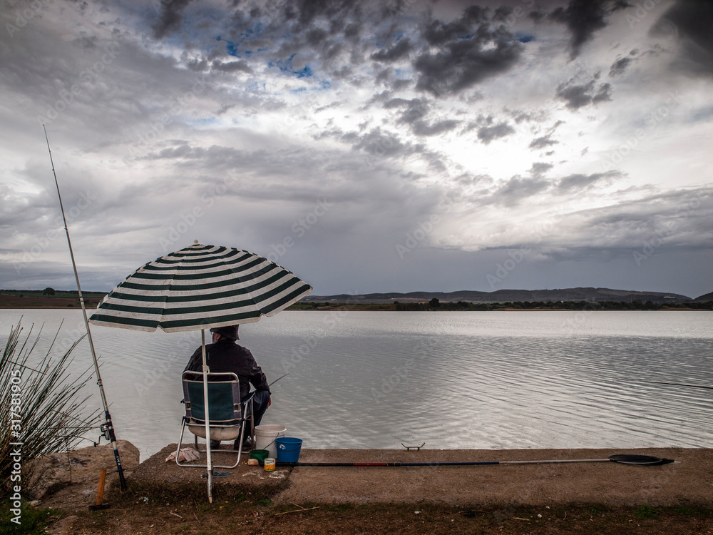 Pescador esperando en la orilla del lago sentado bajo una sombrilla de rayas
