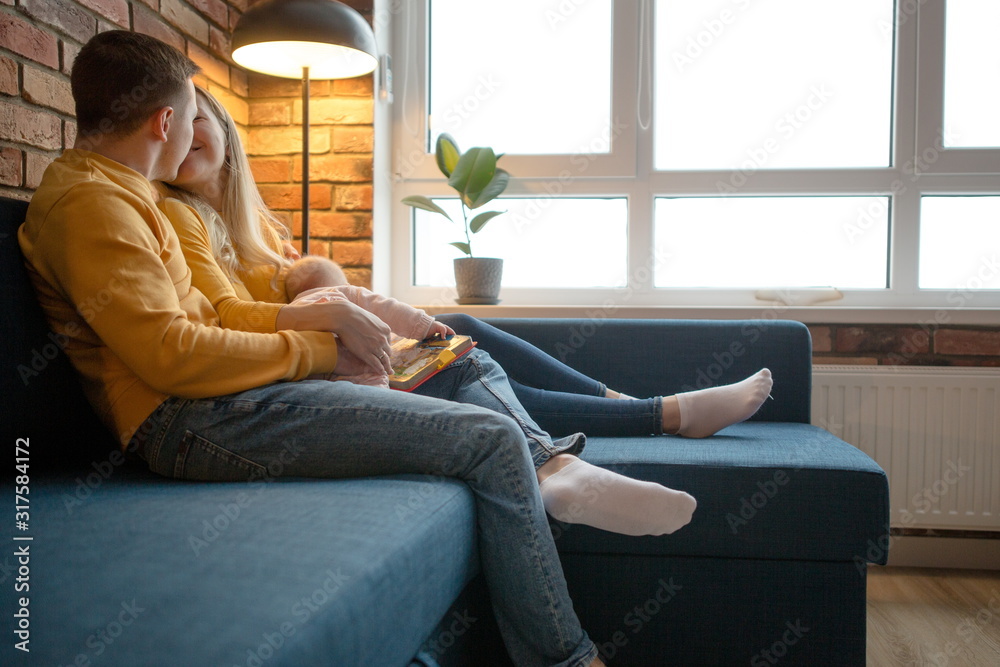 Happy emotions of parents holding a newborn baby sitting on the couch kissing each other Happy emotions of parents holding a newborn baby sitting on the couch kissing each other