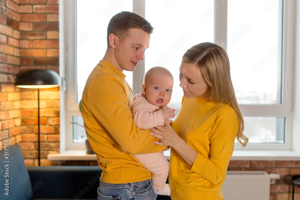 Young family holding a newborn baby standing in a new apartment close up Young family holding a newborn baby standing in a new apartment close up