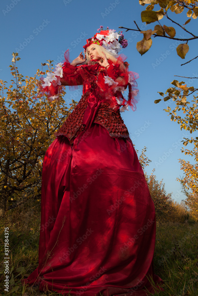 Sensual blond girl in fantasy red fairy tale stylization in apple park.