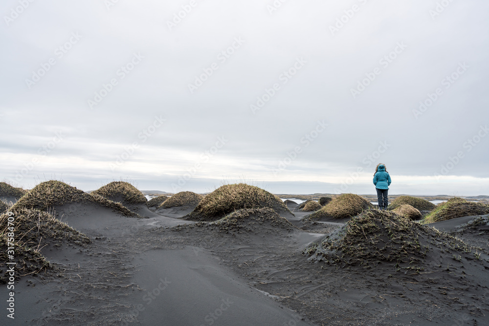 Obraz premium Girl with blue jacket are standing on a sand dune in Stokksnes looking at the view. Icelandic and travel concept.