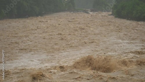 Fast flowing raging river. Soil and mud is moving towards down. After strong rain. Giant roiling brown muddy water. Foamy stream dangerous wild brook. Swollen boiling creating. Damage environmentally.