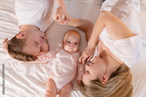Happy family lying on a bed with a baby top view