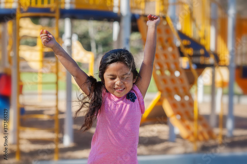 A cute latino girl jumping with joy as she plays in a kids playground. photo