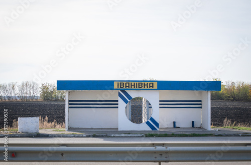 Bus stop Ivanivka on the other side of the road in Ukraine.Traditional structure stop for passengers in a countryside. Shelter along the road.with autumn background. photo