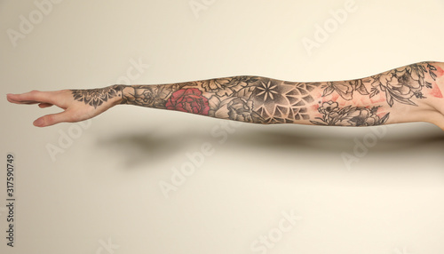 Woman with colorful tattoos on arm against white background, closeup photo